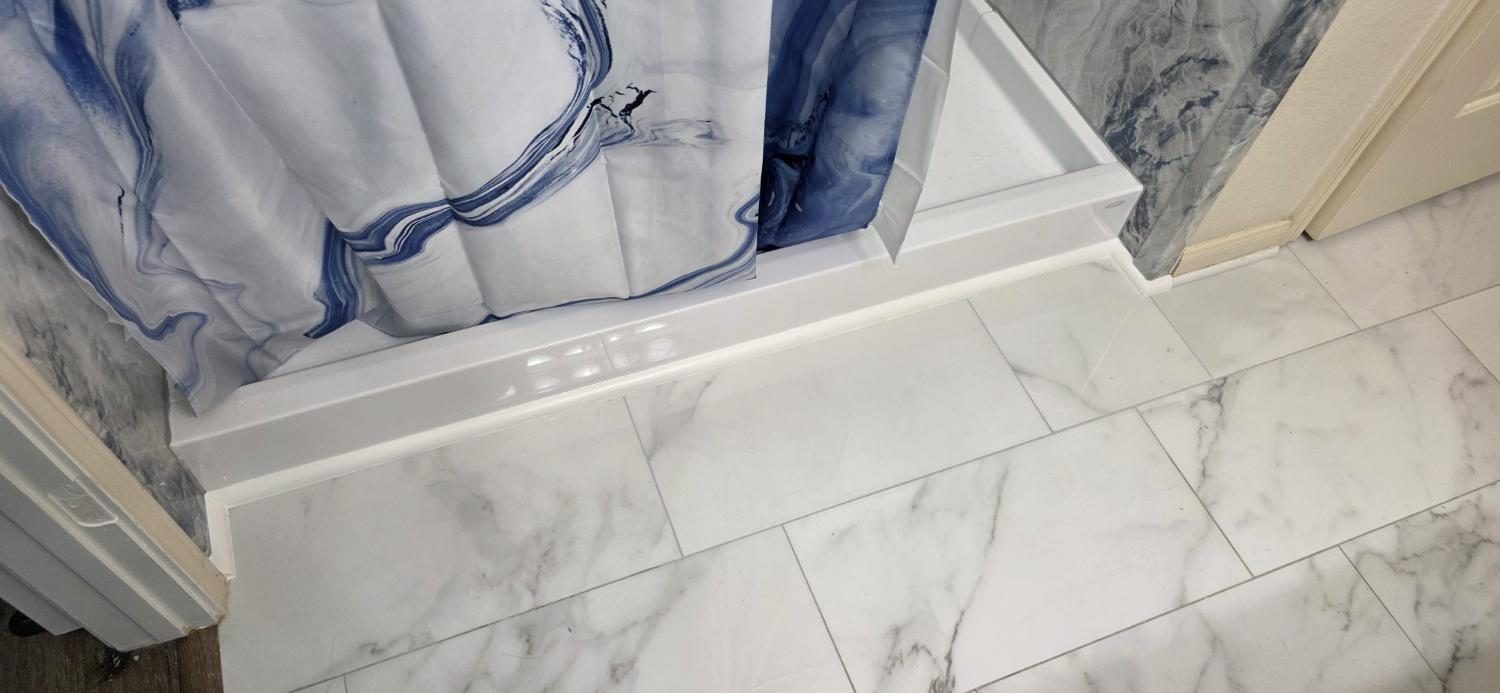 Finished marble-look floor tile around a white shower pan.